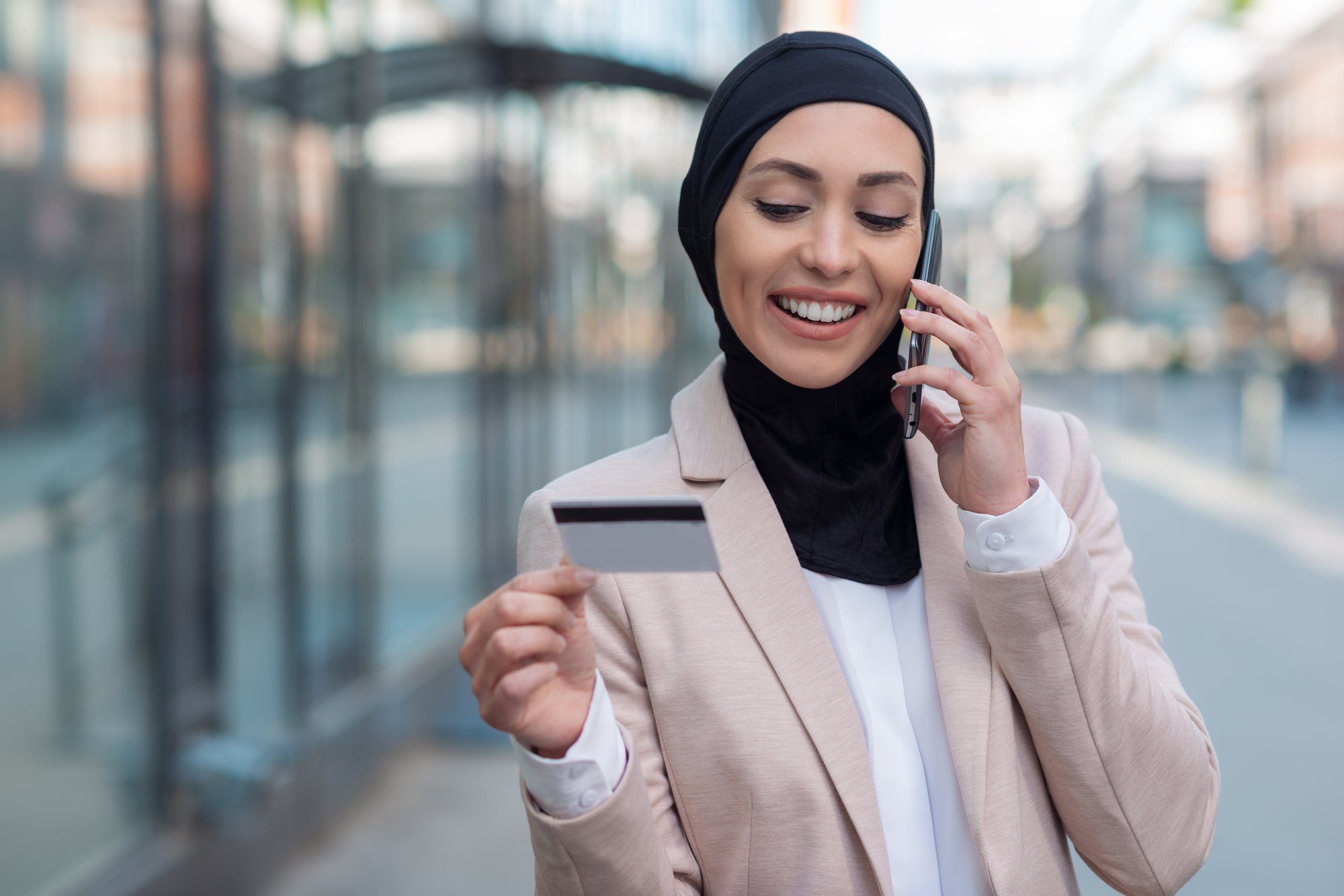 mujer-de-negocios-arabe-hablando-por-telefono-y-sosteniendo-una-tarjeta-de-credito-al-aire-libre
